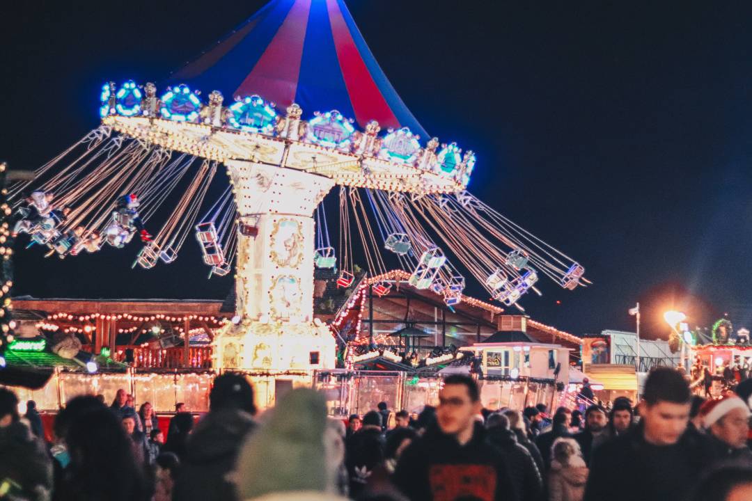 A picture of people at Winter Wonderland at night, with a giant spinning wheel in the background