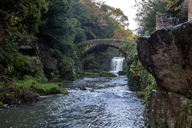 Ancient stone bridge over a river with a small waterfall in the background