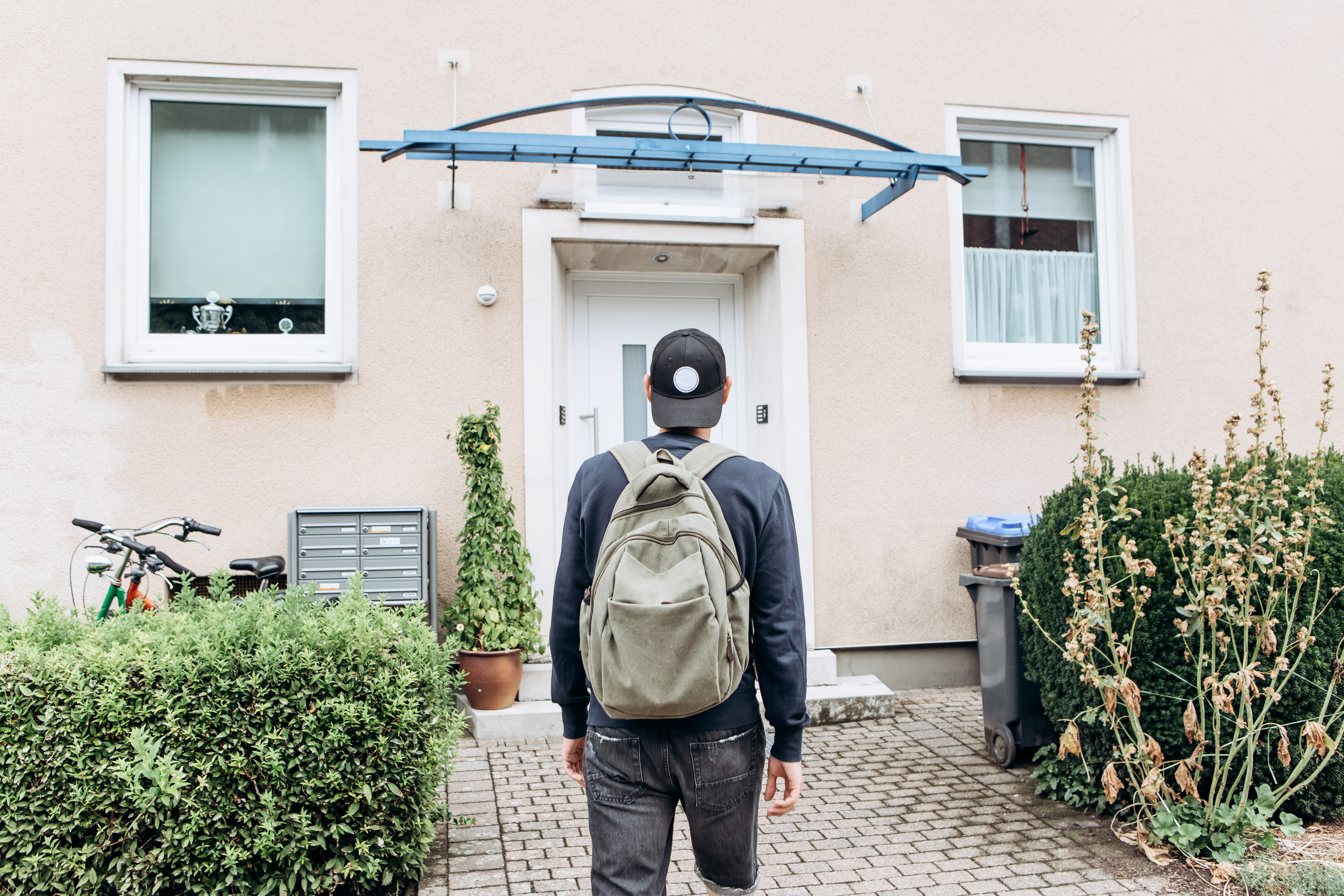 Man wearing a backpack and standing in front of a house
